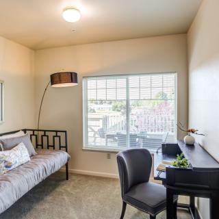 A cozy bedroom with a bed, desk, and chair next to a large window.
