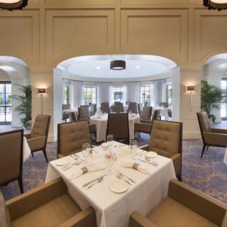 An elegant dining room with neatly set tables and comfortable chairs, featuring large windows that let in natural light.
