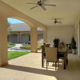 A spacious patio with a dining set, ceiling fans, and a view of the garden.