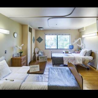 A hospital room with two patient beds, medical equipment, and a window offering natural light.