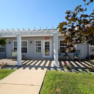 A cozy house with a pergola-covered porch and a pathway leading through the front yard on a sunny day.