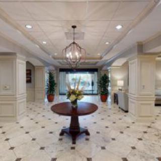 A luxurious lobby with a marble floor, elegant chandelier, and decorative plants.