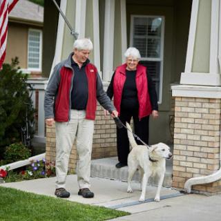An elderly couple enjoying a sunny day outside their home with their dog.