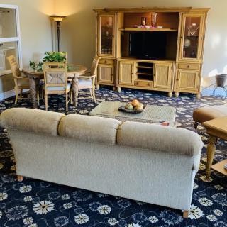 A cozy living room with a central sofa, wooden entertainment center, and patterned carpet.