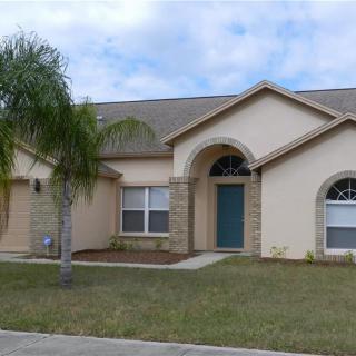 A single-story suburban house with a palm tree in the front yard on a cloudy day.