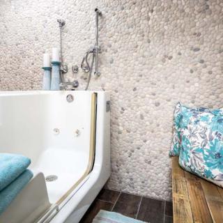 A modern bathroom with a sleek bathtub, mosaic wall tiles, and soft blue towels.