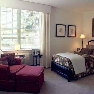 A cozy bedroom interior with a bed, a red armchair, and a window letting in natural light.
