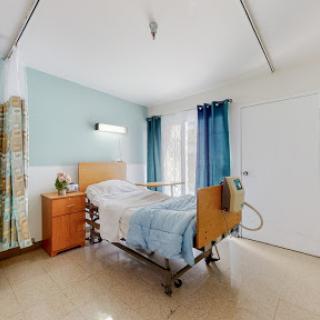 A well-lit hospital patient room featuring a bed, dresser, and curtains.