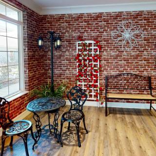 A cozy indoor space with a brick wall, featuring a metal table and chairs, a wooden bench, and decorative elements.