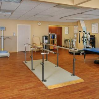 A rehabilitation room equipped with parallel bars and various physical therapy equipment.