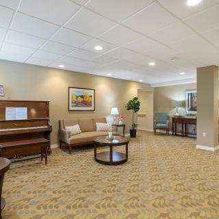 A spacious lounge area featuring a piano, sofa, and coffee table with artwork on the walls.