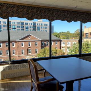 A sunlit room with a table overlooking a view of buildings and trees.