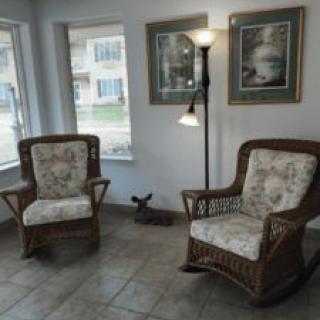 A cozy living room corner featuring two rattan chairs with floral cushions, a floor lamp, and framed artwork on the walls.