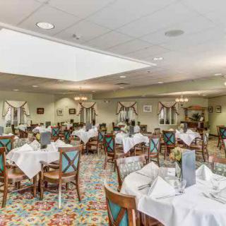A spacious and elegantly decorated restaurant dining room with neatly arranged tables and chairs, featuring white tablecloths and set for dining.