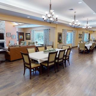 A spacious dining room with elegantly set tables and chandeliers, featuring wooden flooring and large windows.