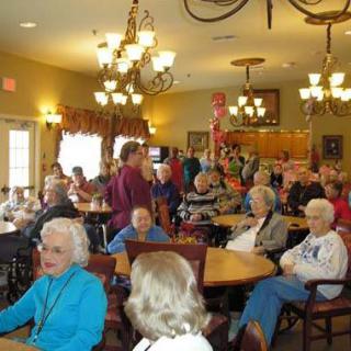A lively gathering of seniors in a community room with chandeliers overhead.