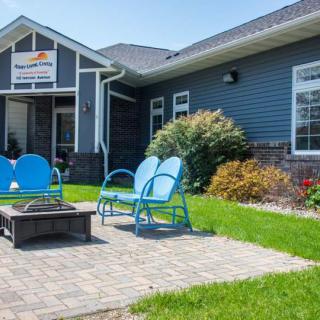 A cozy outdoor seating area with blue chairs and a fire pit in front of a building.