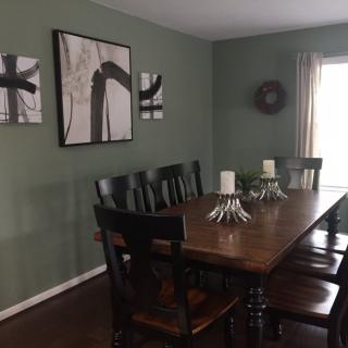 A dining room featuring a wooden table with chairs, adorned with candles and abstract artwork on green walls.