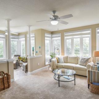 A bright and spacious living room with large windows, featuring a comfortable sofa, coffee table, and a ceiling fan.