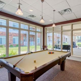 A well-lit recreation room with a pool table and large windows.