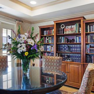 A cozy library with a round table, floral arrangement, and bookshelves filled with books.