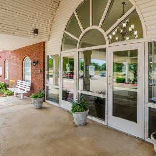 A welcoming entrance to a building featuring large glass doors and decorative planters under a covered porch.