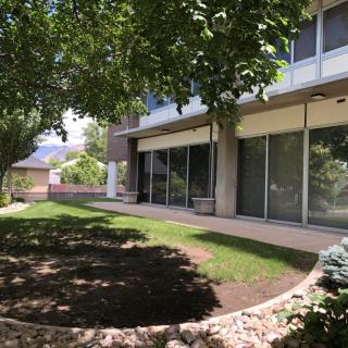 A modern building with a patio, surrounded by a well-maintained lawn and trees on a sunny day.