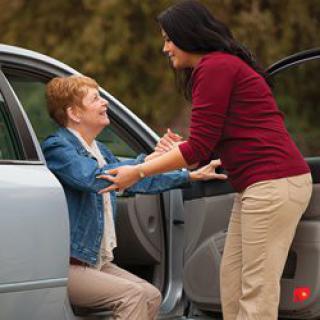 A woman assisting an elderly person out of a car.