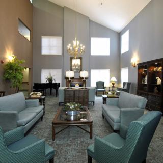 A spacious living room with elegant furniture, chandelier lighting, and a grand piano.