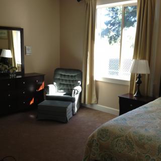 A cozy bedroom with a dresser, armchair, and a window letting in natural light.
