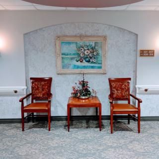 A neatly arranged interior setting featuring two chairs flanking a small table with floral decorations beneath a wall painting.