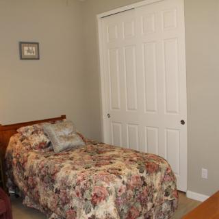 A cozy bedroom with a single bed adorned with floral bedding, featuring a closet and neutral-colored walls.