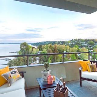 A cozy balcony setup with outdoor furniture overlooking a beautiful lake and lush greenery.