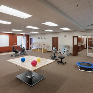 A spacious therapy room equipped with various fitness and rehabilitation tools, including exercise balls, workout machines, and a trampoline.