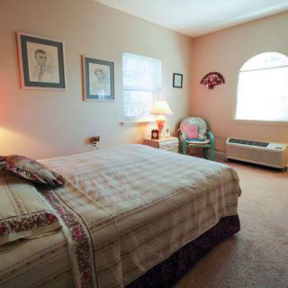 A cozy bedroom with a large bed, bedside lamp, and natural light from windows.