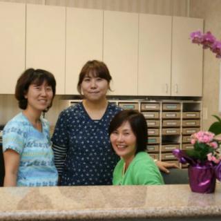 Three people posing behind a reception desk with flowers.