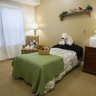 A cozy bedroom with a single bed, featuring stuffed animals and a bedside lamp.