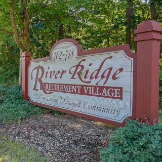 Entrance sign for River Ridge Retirement Village surrounded by greenery.