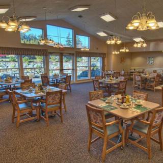 A cozy restaurant dining area with neatly arranged tables and chairs, illuminated by chandeliers and natural light from large windows.