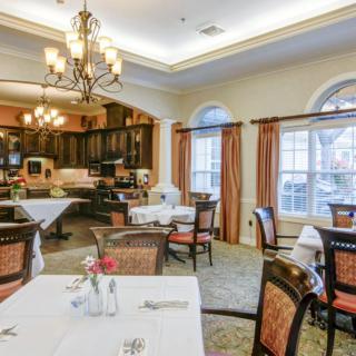 An elegant dining room with neatly arranged tables and chairs, featuring a warm ambiance with chandeliers and large windows.