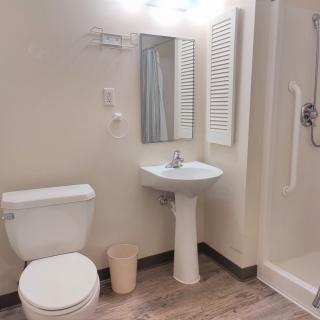 A clean, modern bathroom with a toilet, pedestal sink, mirror, and shower.