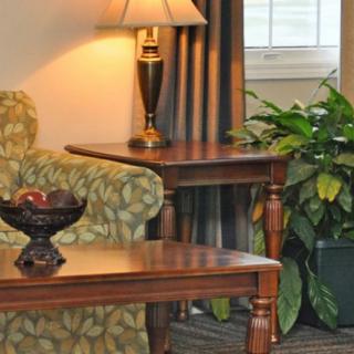 A cozy living room corner with a wooden table, lamp, and green plant beside a patterned sofa.