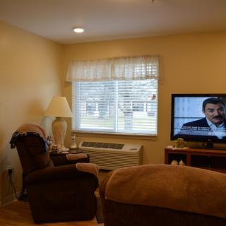 A cozy living room with a television, a comfortable chair, and a window letting in natural light.
