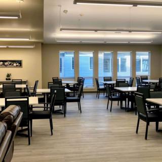 An empty dining room with neatly arranged tables and chairs, illuminated by overhead lights.