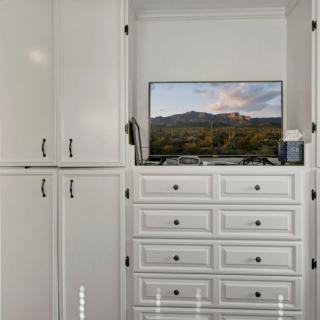 A neatly organized white cabinet with multiple drawers, featuring a television on top displaying a scenic landscape.