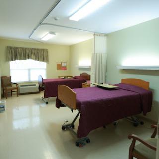 A simple patient room in a hospital with two beds and basic furnishings.