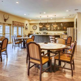 A spacious dining and kitchen area with multiple tables and chairs, featuring a hardwood floor and modern lighting.