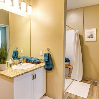 A modern bathroom featuring a sink, mirror, and shower area with teal towels and light decor.