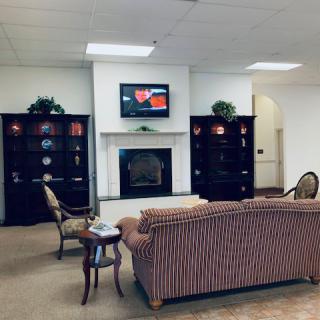 A cozy living room featuring a striped sofa, armchairs, and a television mounted above a fireplace, flanked by decorative shelves.