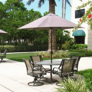 A serene outdoor patio area with a table, chairs, and an umbrella surrounded by lush greenery.
